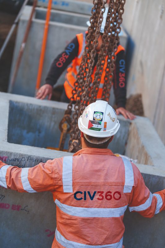 Two workers in CIV360 hi-vis guiding a precast concrete pit being lowered on lifting chains