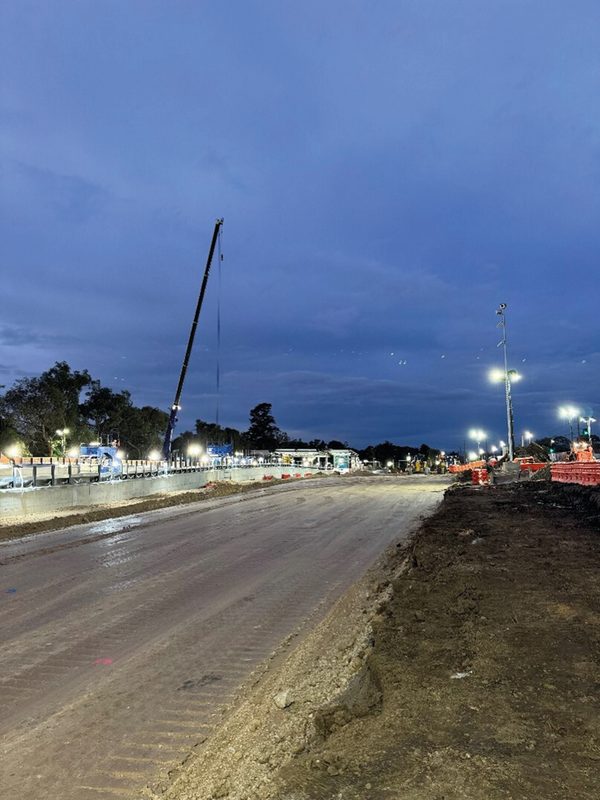 Road formation at dusk with a mobile crane and a floodlit construction site behind