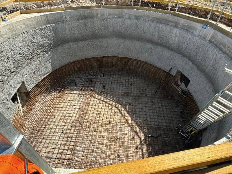 Looking down into a circular shotcrete-lined shaft with reinforcement mesh laid across the base