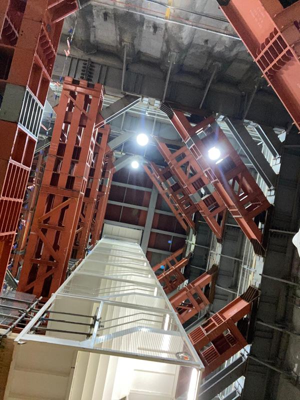 Looking up the shaft past tiers of red steel props and a caged stair tower