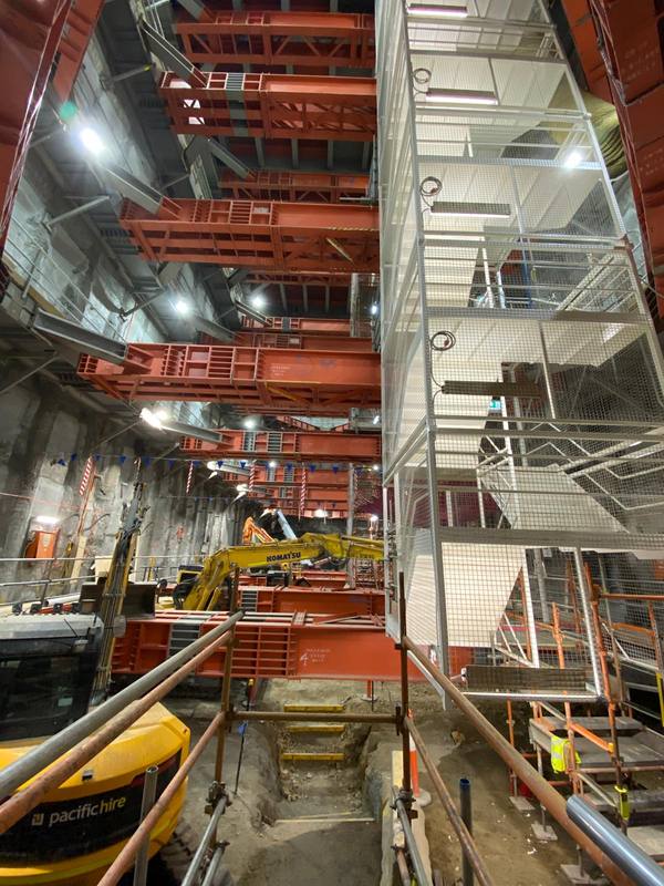 Excavators working at the base of the shaft beneath tiers of red steel props, beside a caged stair tower