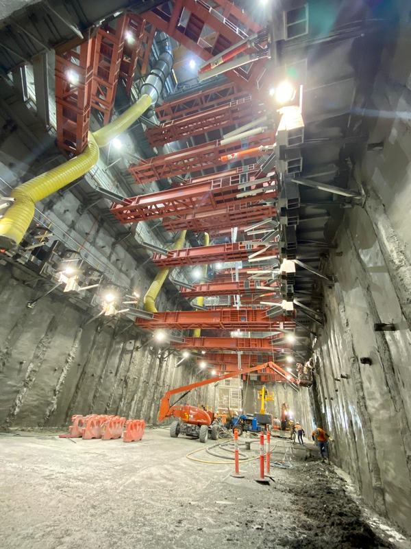 Crew working at the base of a deep shotcrete-lined excavation under tiers of red steel props and yellow ventilation ducting