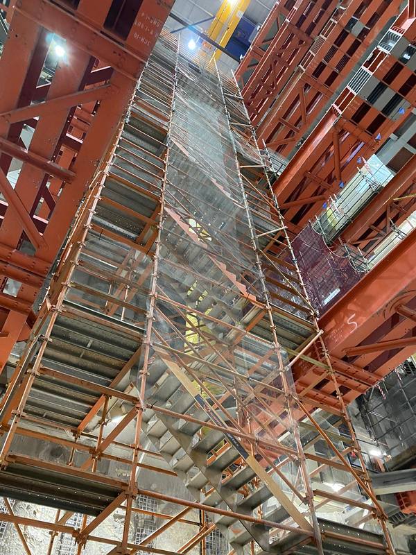 Scaffold stair tower rising through tiers of red steel props in the shaft
