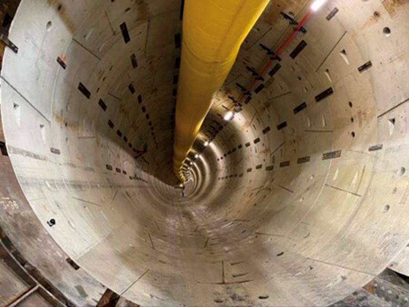 View along a bored tunnel lined with precast concrete segments and a yellow ventilation duct
