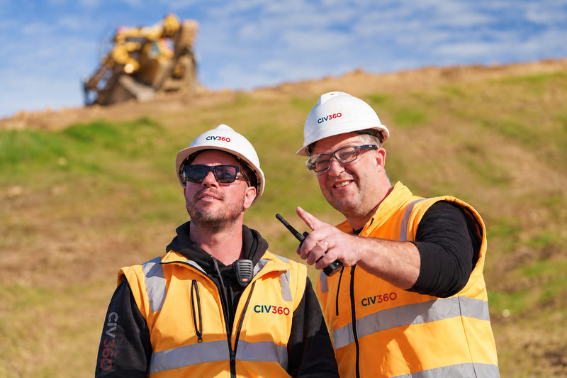 Two CIV360 supervisors in hi-vis, one pointing across the site, with a dozer on the embankment behind