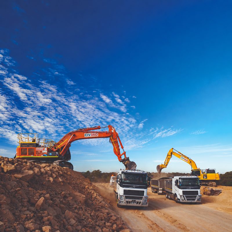 Two CIV360 excavators loading truck and dog trailers on a rock earthworks site under a deep blue sky