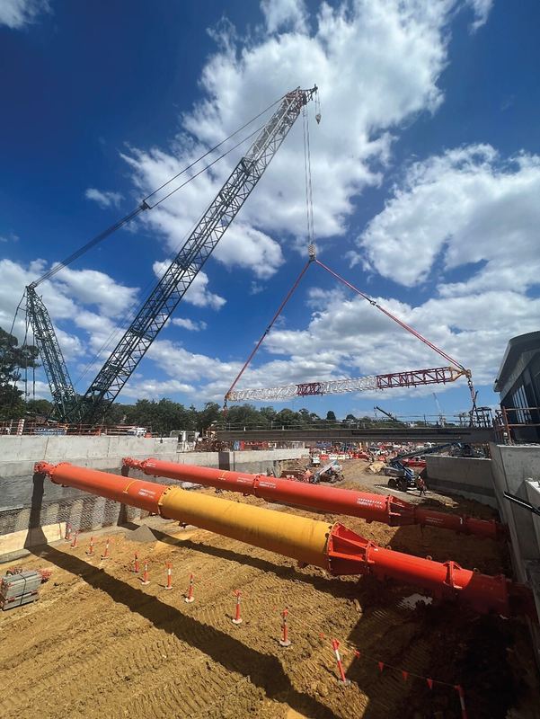Crawler crane lifting a steel strut frame over a braced excavation with large orange props
