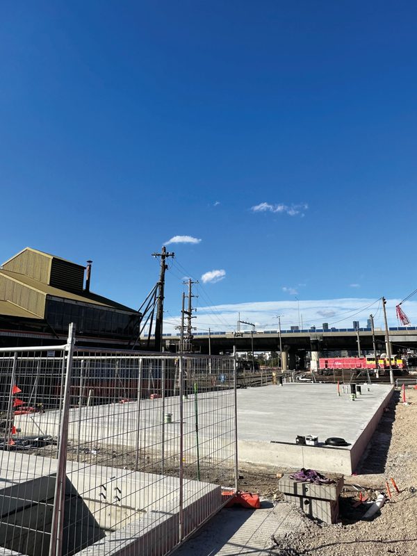 Newly completed concrete slab inside temporary fencing at a rail maintenance yard, with the freeway and city towers behind